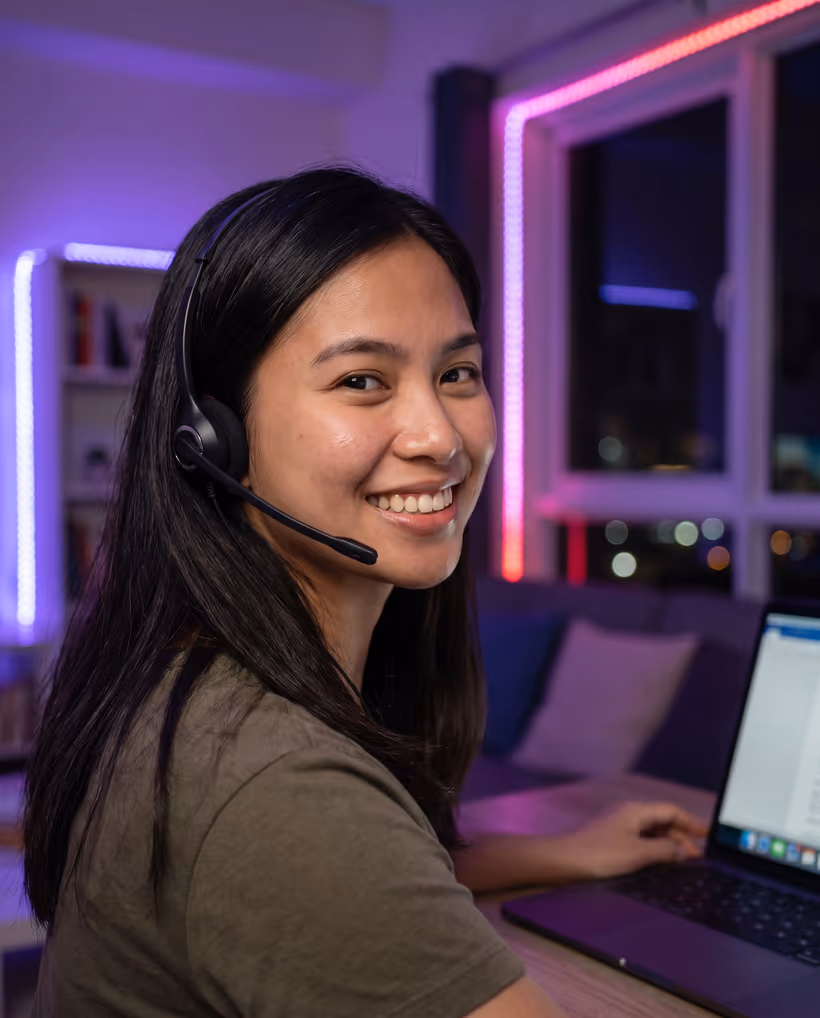 A virtual assistant in a headset smiling at her desk