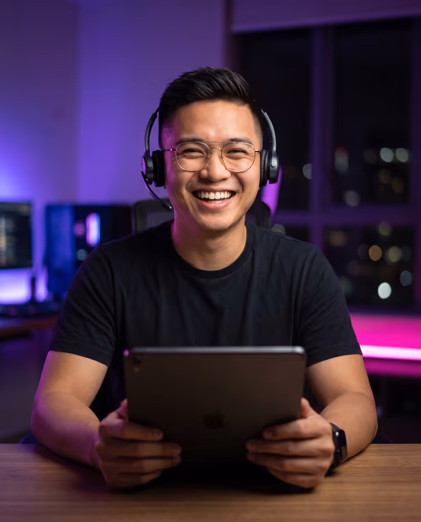 An assistant in a headset laughing while holding a tablet at his desk